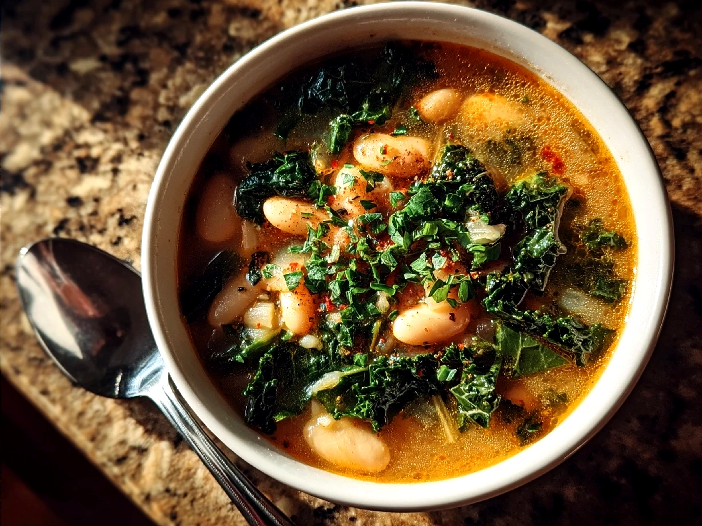 A bowl of creamy White Bean Kale Soup garnished with olive oil and Parmesan cheese